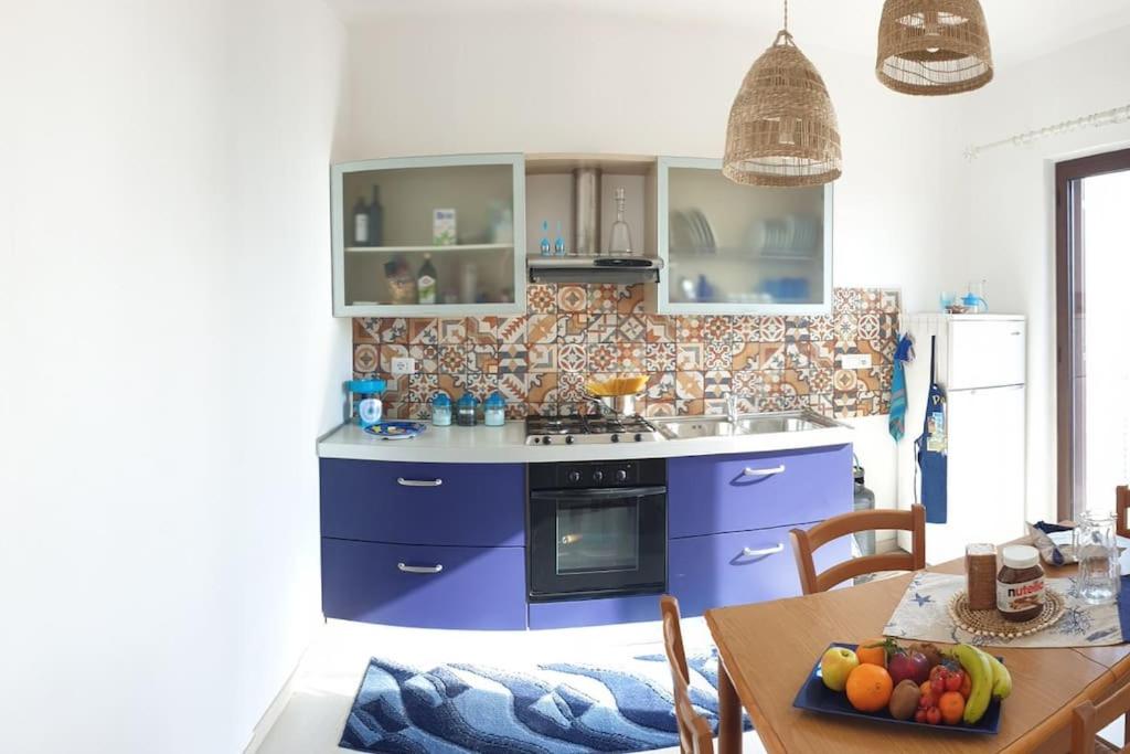 a kitchen with blue cabinets and a table with a bowl of fruit at RgB_Apartments in Lampedusa