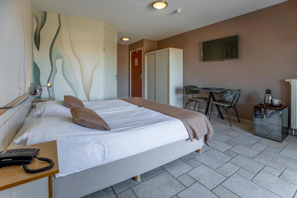 een slaapkamer met een bed, een tafel en een televisie bij Hotel Tesselhof in De Koog