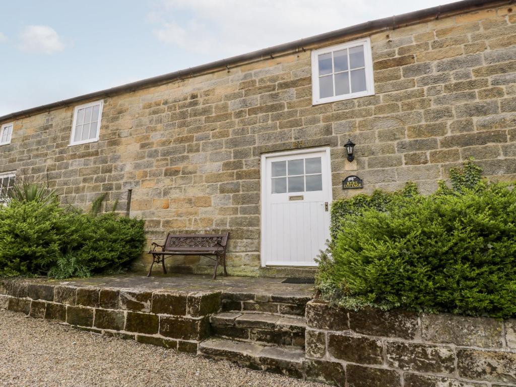 a brick building with a white door and a bench at Byre Cottage in Whitby