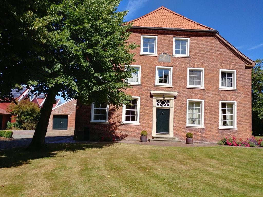 een grote bakstenen huis met een boom in de tuin bij Ferienwohnung im idyllischen Gulfhof in Krummhörn