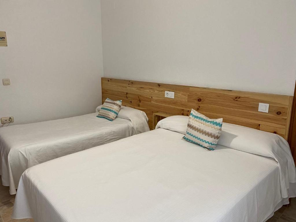 2 bedden in een kamer met witte lakens en blauwe kussens bij Hostal Barbate in Barbate