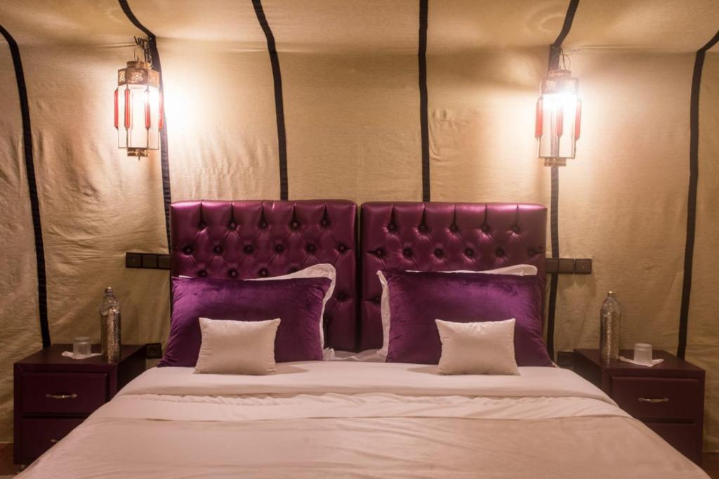 a bed with a purple headboard and purple pillows at Luxury Desert Camp Amanar in Merzouga