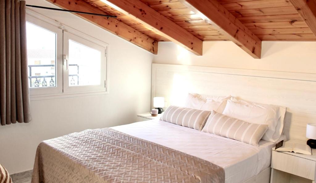 a bedroom with a white bed and two windows at Lightful Attic at Regina Apartments in Alikanas