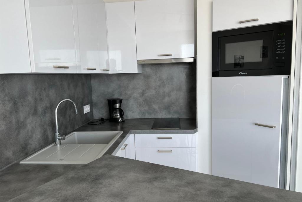 a kitchen with white cabinets and a sink and a microwave at Les Pieds dans le Sable in Le Grau-du-Roi