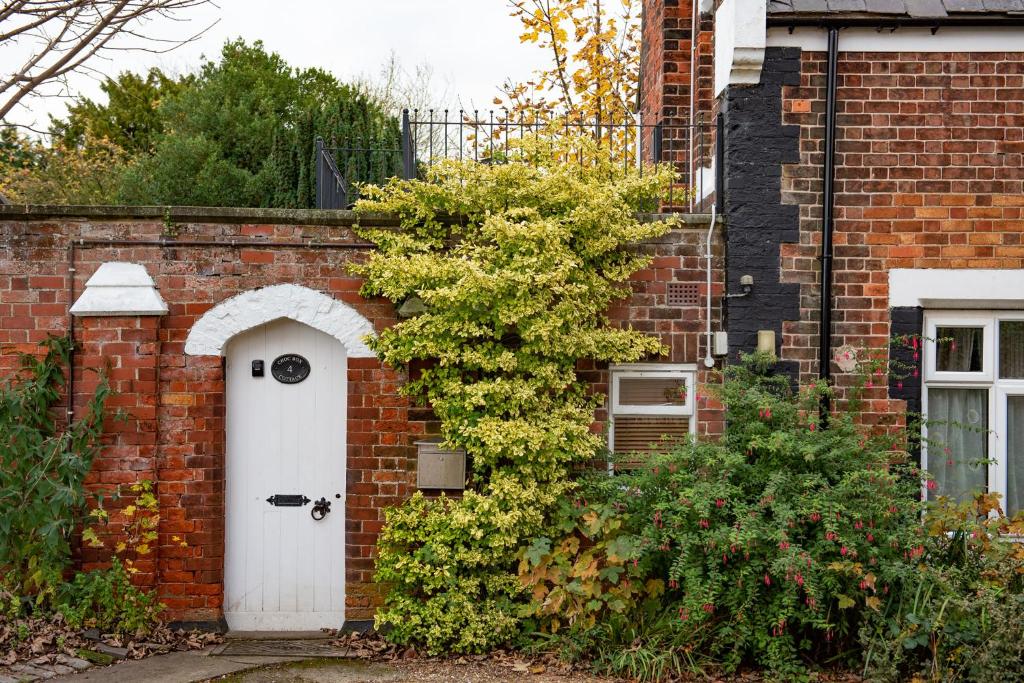 a brick house with a white door and a bush at Chocbox Cottage - 2 bedroom chocbox cottage with hottub and log fire in Pocklington