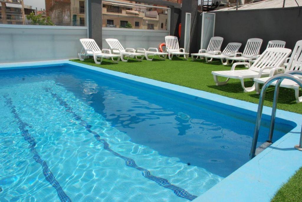 a pool with white chairs and a group at Hotel Armonía in Lloret de Mar