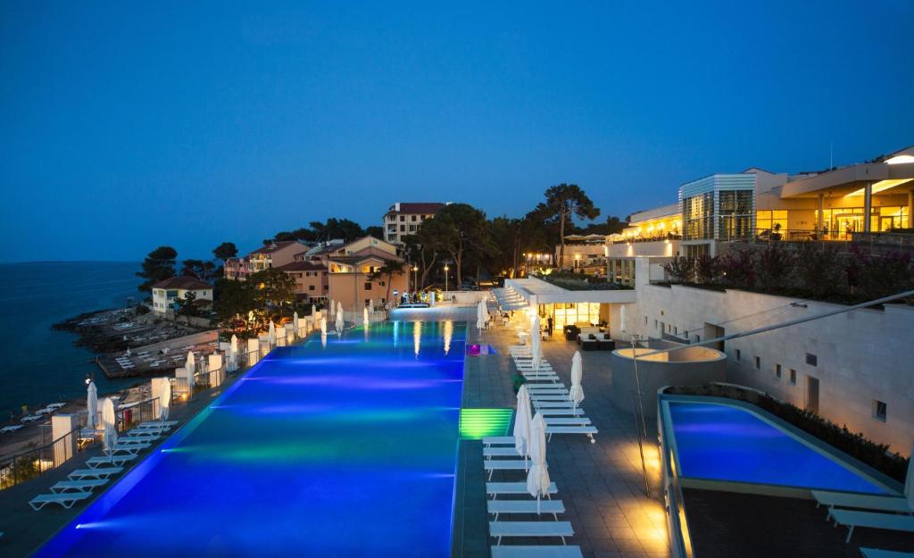 ein großer Pool in der Nacht mit dem Meer in der Unterkunft Vitality Hotel Punta in Veli Lošinj