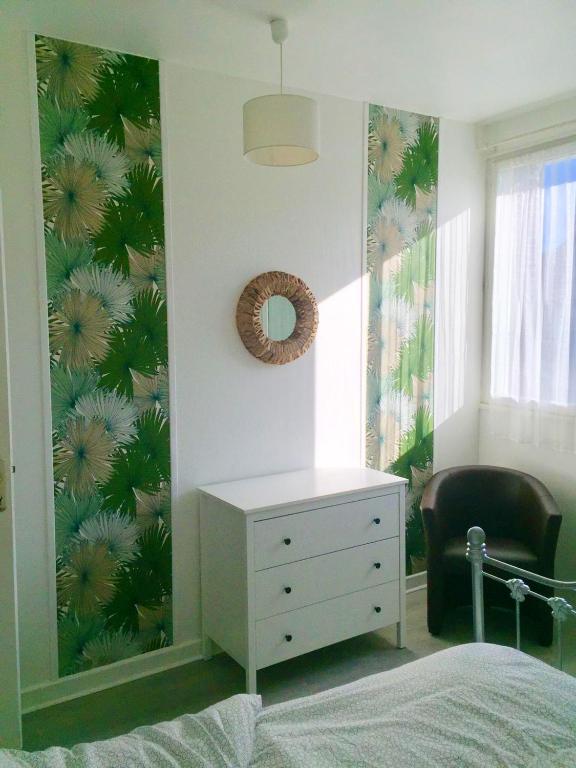 - une chambre avec une commode blanche et un mur orné d'un papier peint tropical dans l'établissement Appartement cosy à Rosny-sous-Bois 42 m² avec parking, à Rosny-sous-Bois