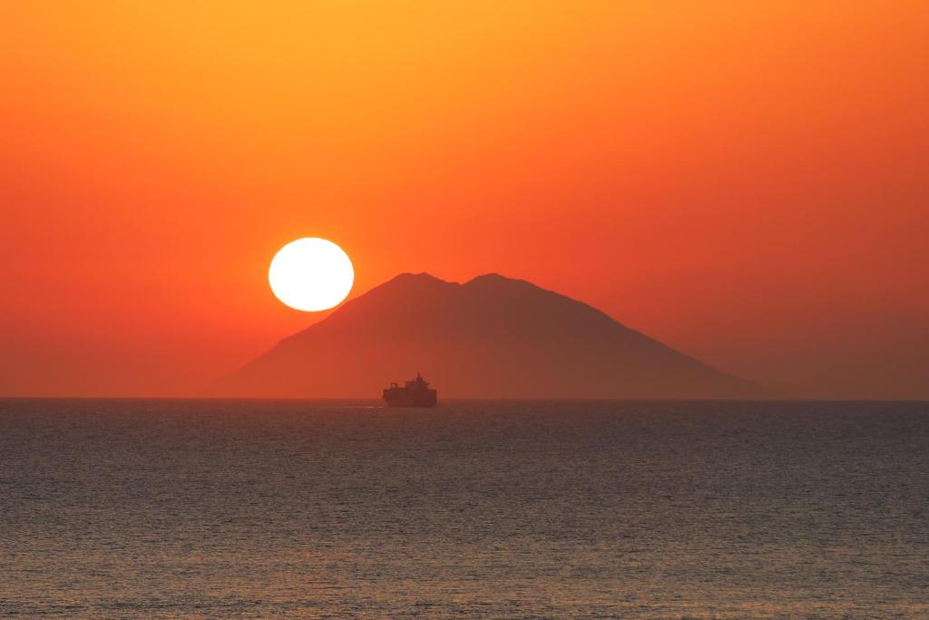 een boot in de oceaan bij zonsondergang met een berg bij Deus Accomodation in Tropea