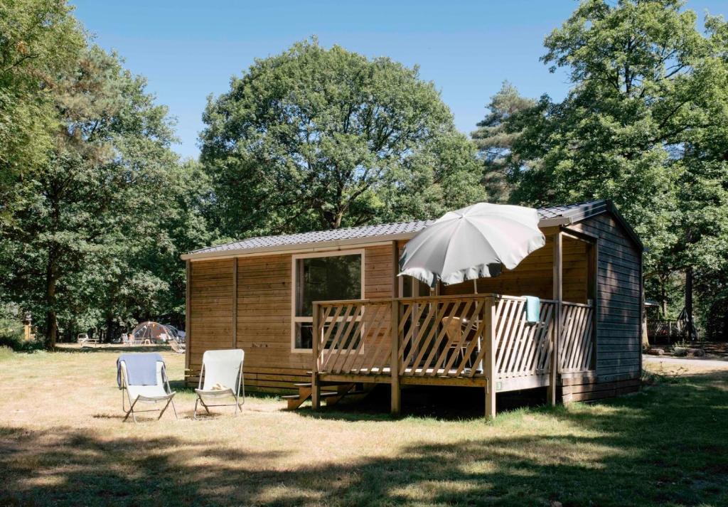 a small cabin with two chairs and an umbrella at Huttopia Lac de Sillé in Sillé-le-Guillaume