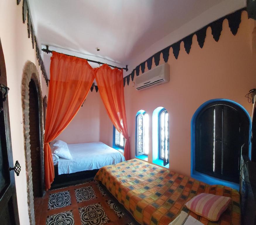 1 dormitorio con 2 camas y cortinas de color naranja en Dar Zman, en Chefchaouen