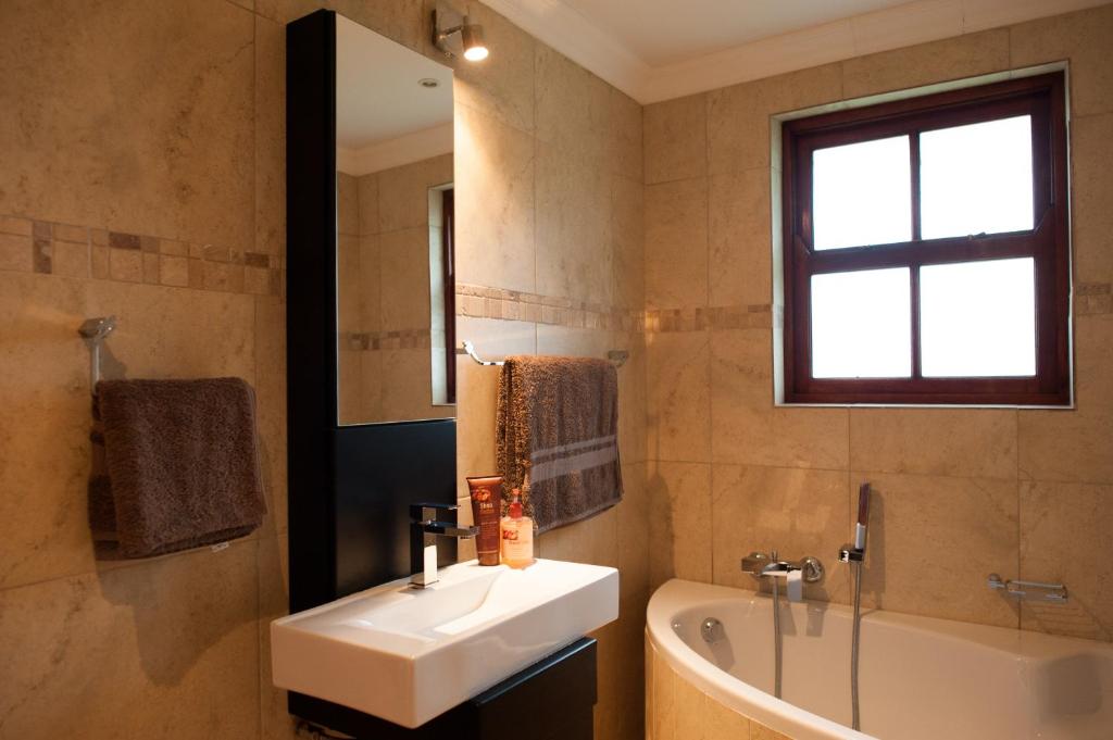 La salle de bains est pourvue d'un lavabo, d'une baignoire et d'un miroir. dans l'établissement Strawberry Fields Country Manor Guest House, à Johannesbourg