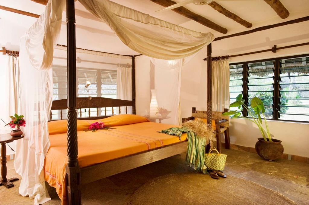1 dormitorio con cama con dosel y sábanas de color naranja en Diani Marine Divers Village, en Diani Beach