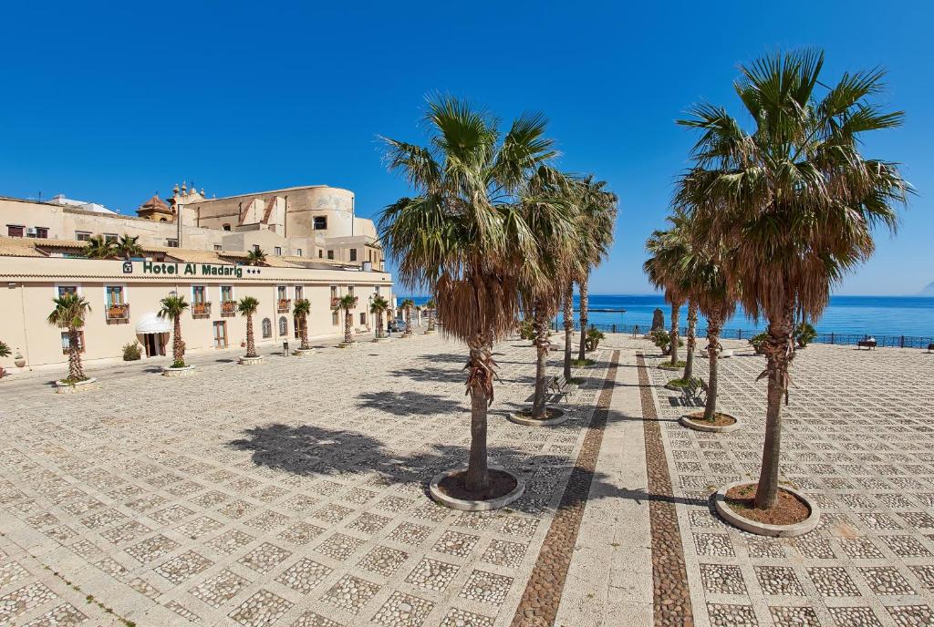 uma fileira de palmeiras num passeio junto ao oceano em Hotel Al Madarig em Castellammare del Golfo