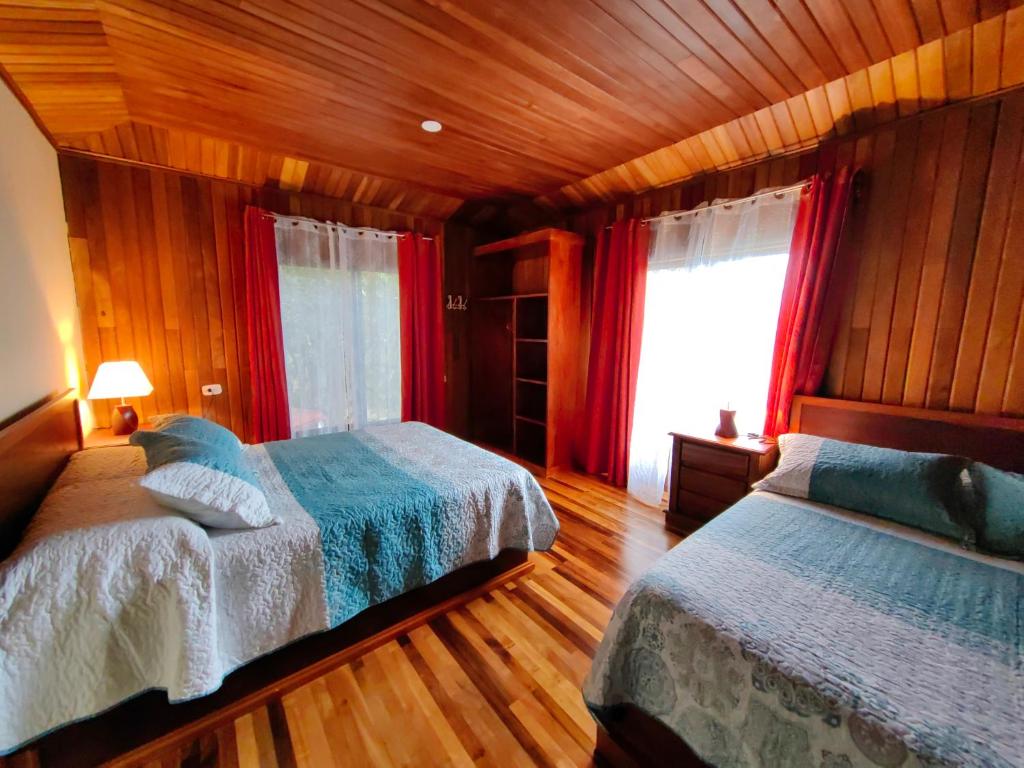 een slaapkamer met 2 bedden en een raam met rode gordijnen bij Monteverde House in Monteverde Costa Rica