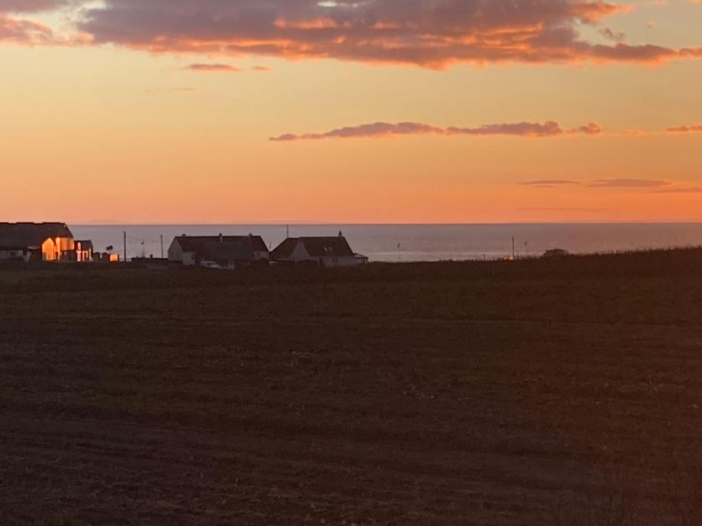 a sunset over a field with houses and the ocean at Luxury caravan at Turnberry - short walk to beach in Girvan
