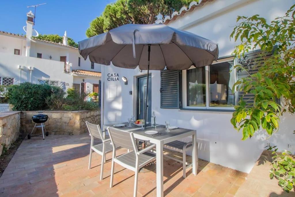 a table and chairs with an umbrella on a patio at Sunny villa by the beach surrounded by pine trees in Vale do Lobo