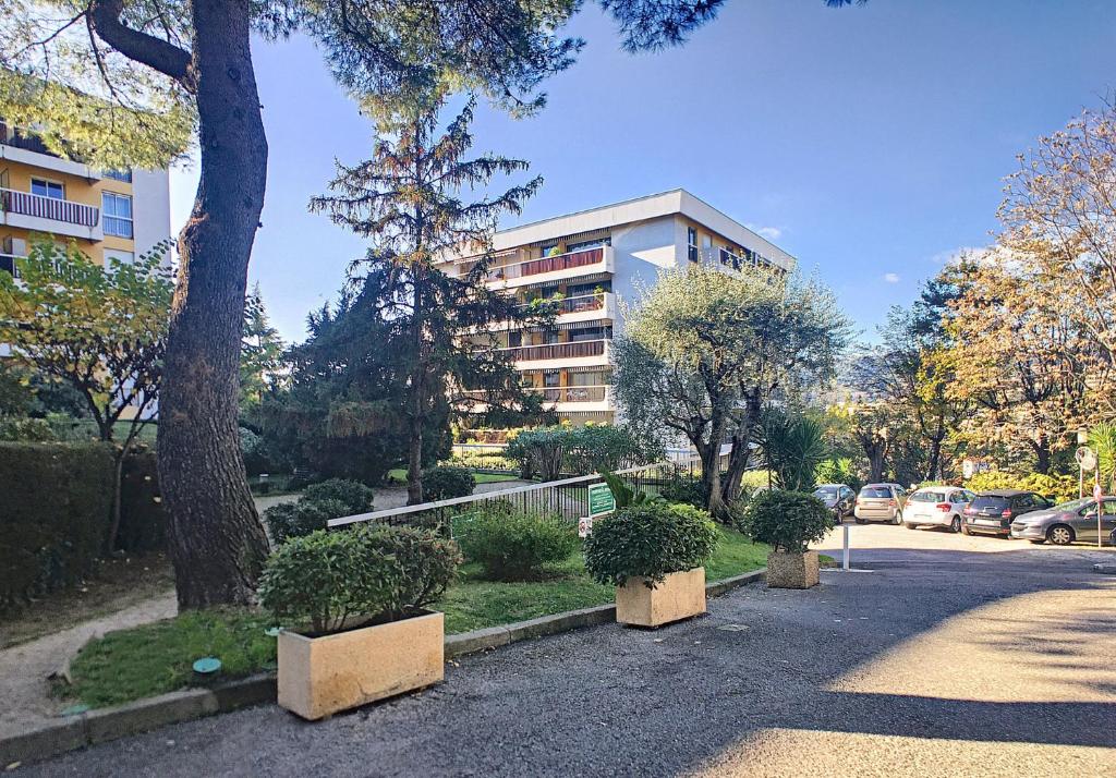 un bâtiment avec des arbres et des buissons en face d'une rue dans l'établissement HOME ET HOLIDAY Le Petit Manseng, à Nice