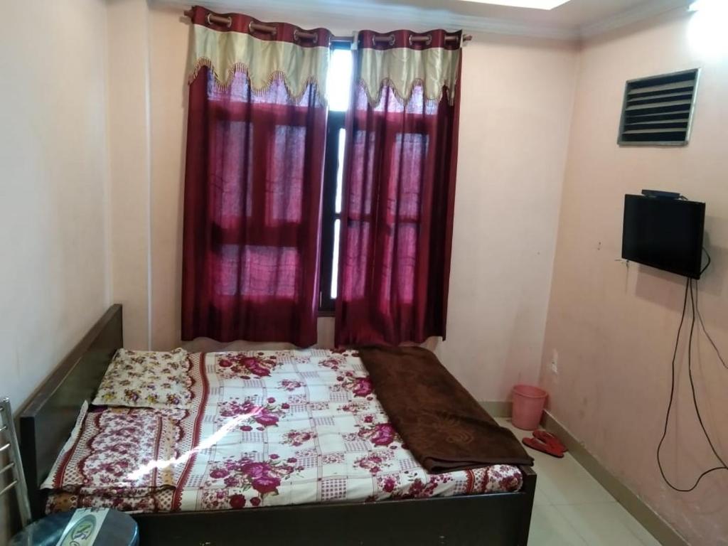 a bedroom with a bed and a window with red curtains at Hotel Hansa Palace by WB Inn in Kānpur