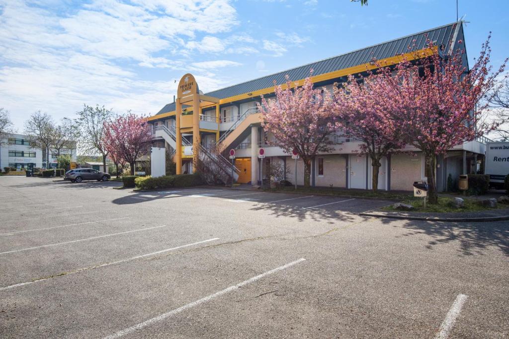 un parcheggio di fronte a un edificio con alberi rosa di Premiere Classe Lyon Est - Bron Eurexpo a Décines-Charpieu