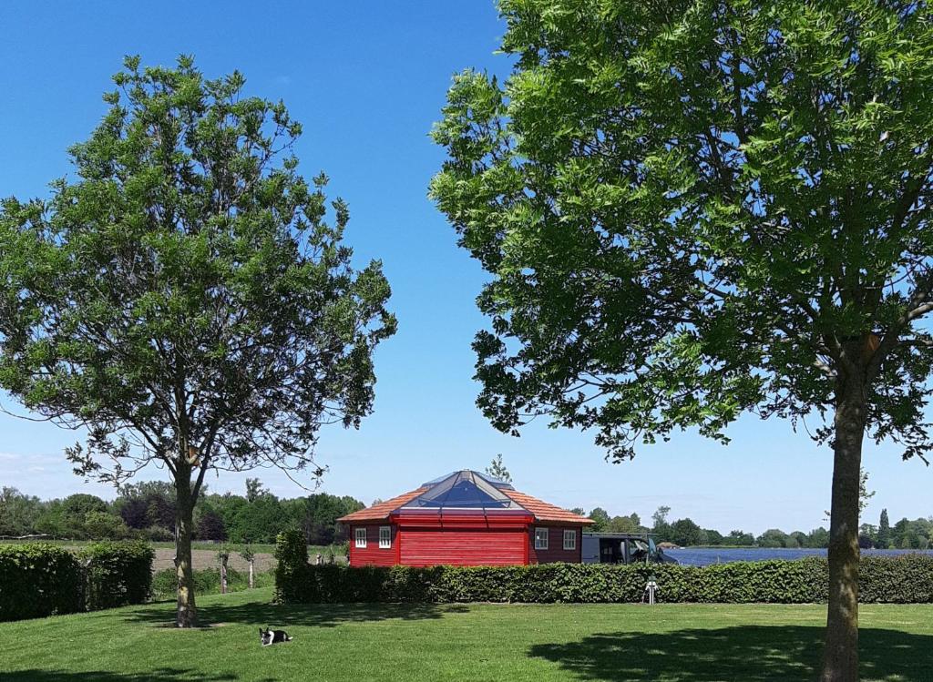 un edificio rosso in un campo con due alberi di Happy Home-Slapen onder de sterren a Kronenberg