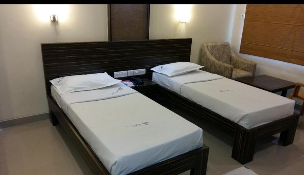 twee bedden in een hotelkamer met een stoel bij Hotel Jaybala International in Kanchipuram