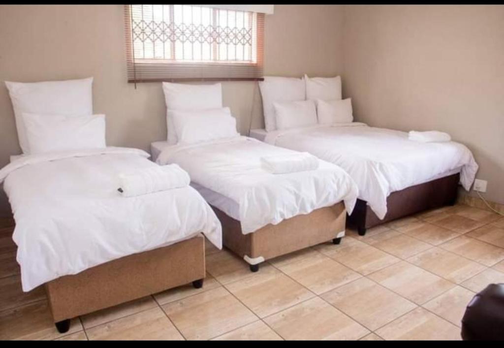 Zimmer mit 3 Betten, weißer Bettwäsche und einem Fenster in der Unterkunft Fairfield Guest House in Pietermaritzburg