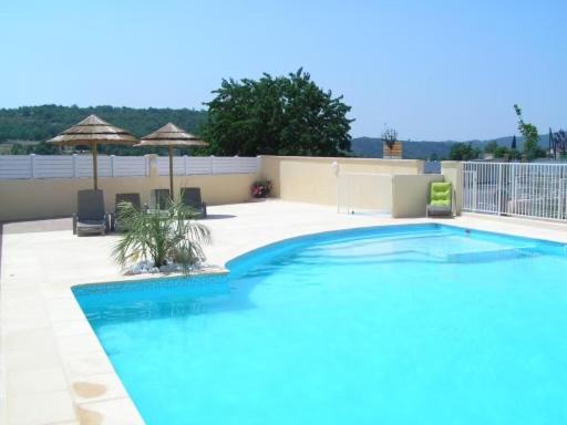 una gran piscina azul en un patio con sombrillas en Aux couleurs d'Ardèche, en Vallon-Pont-dʼArc