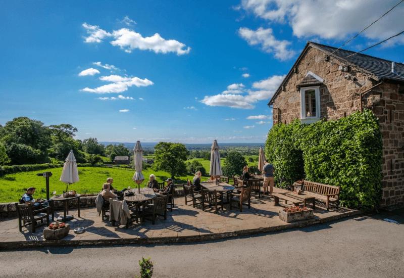 Un groupe de personnes assises à des tables avec des parapluies dans l'établissement The Pheasant Inn, à Higher Burwardsley