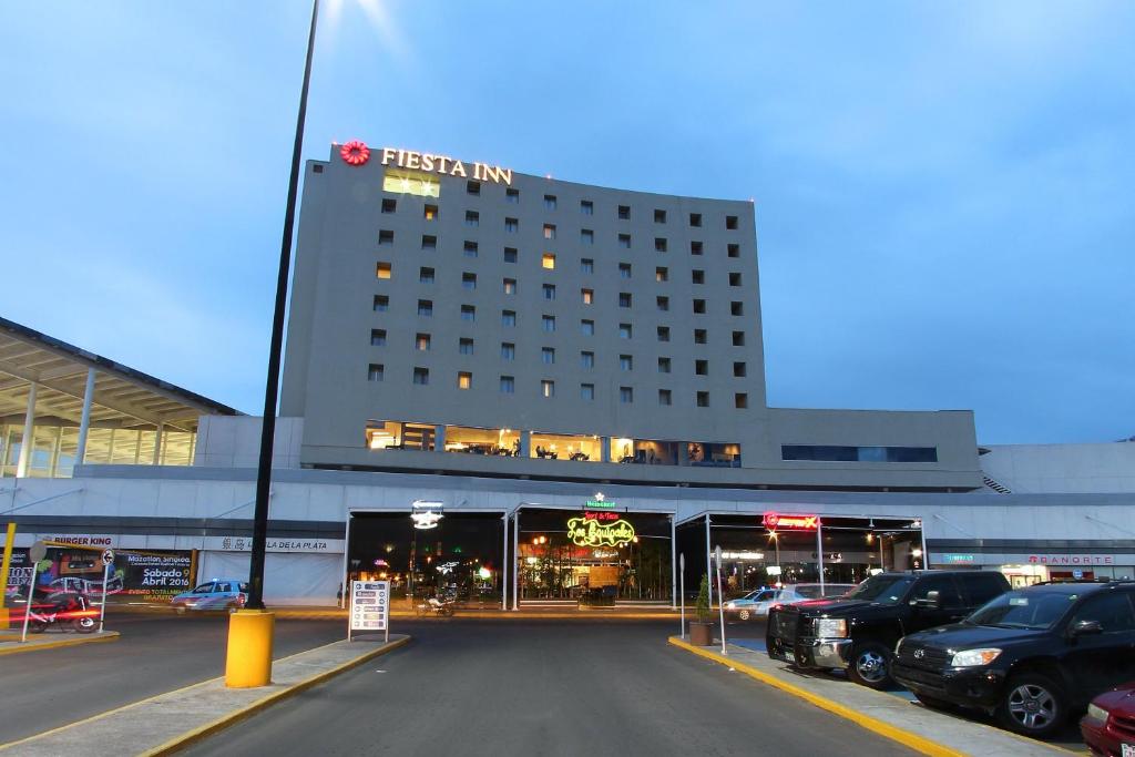 un bâtiment d'hôtel avec des voitures garées dans un parking dans l'établissement Fiesta Inn Durango, à Durango