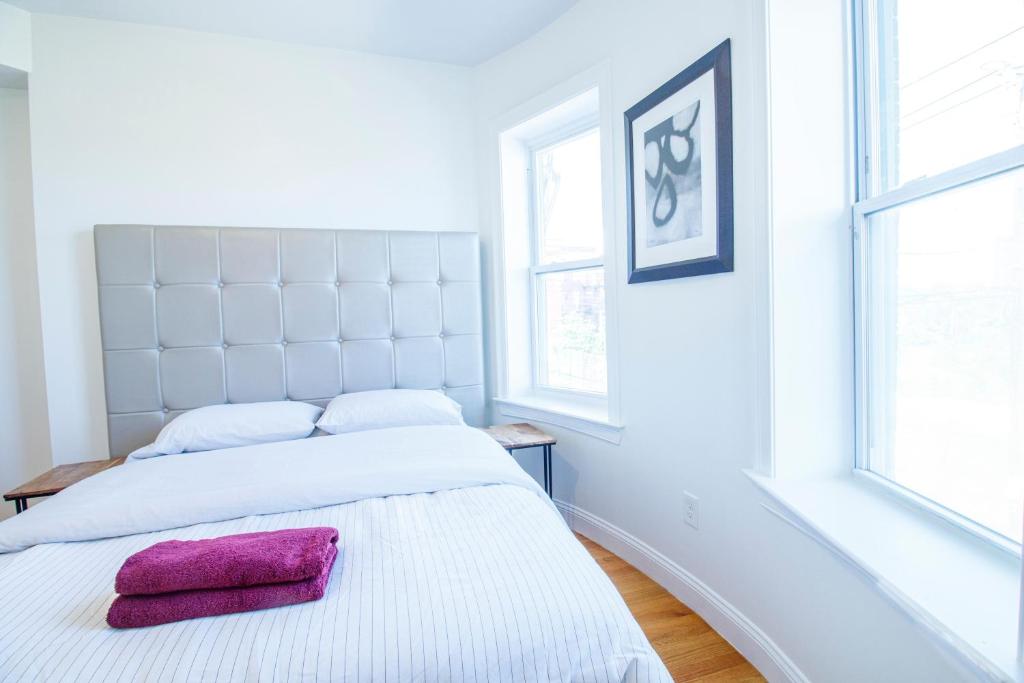 two beds in a white bedroom with a pink towel at 4BR 1,5BH Sunny Apt in Roxbury in Boston