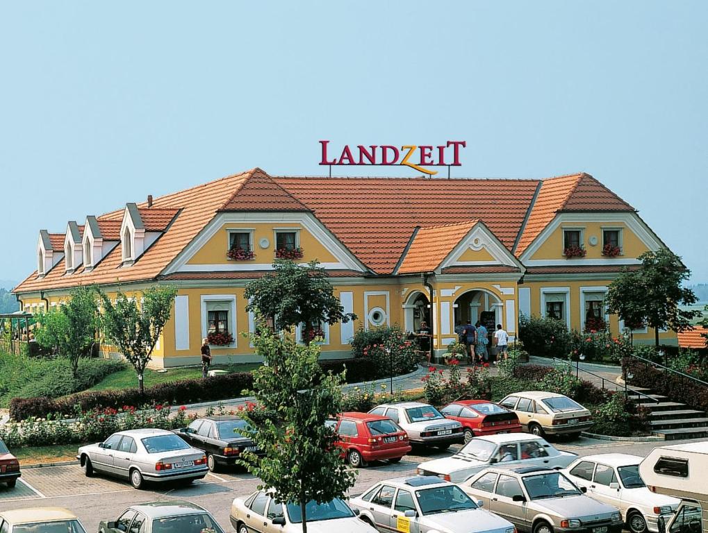 a large yellow building with cars parked in a parking lot at Landzeit Autobahnrestaurant & Motorhotel Loipersdorf in Kitzladen