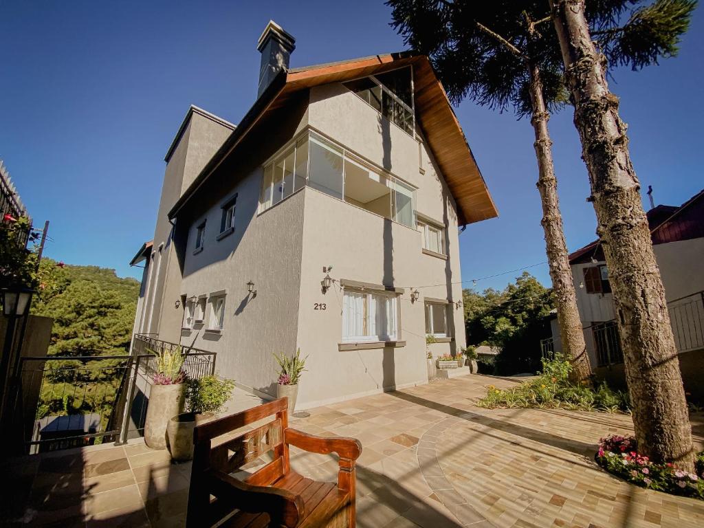 une maison blanche avec un arbre et un banc dans l'établissement Villary Flats Gramado, à Gramado