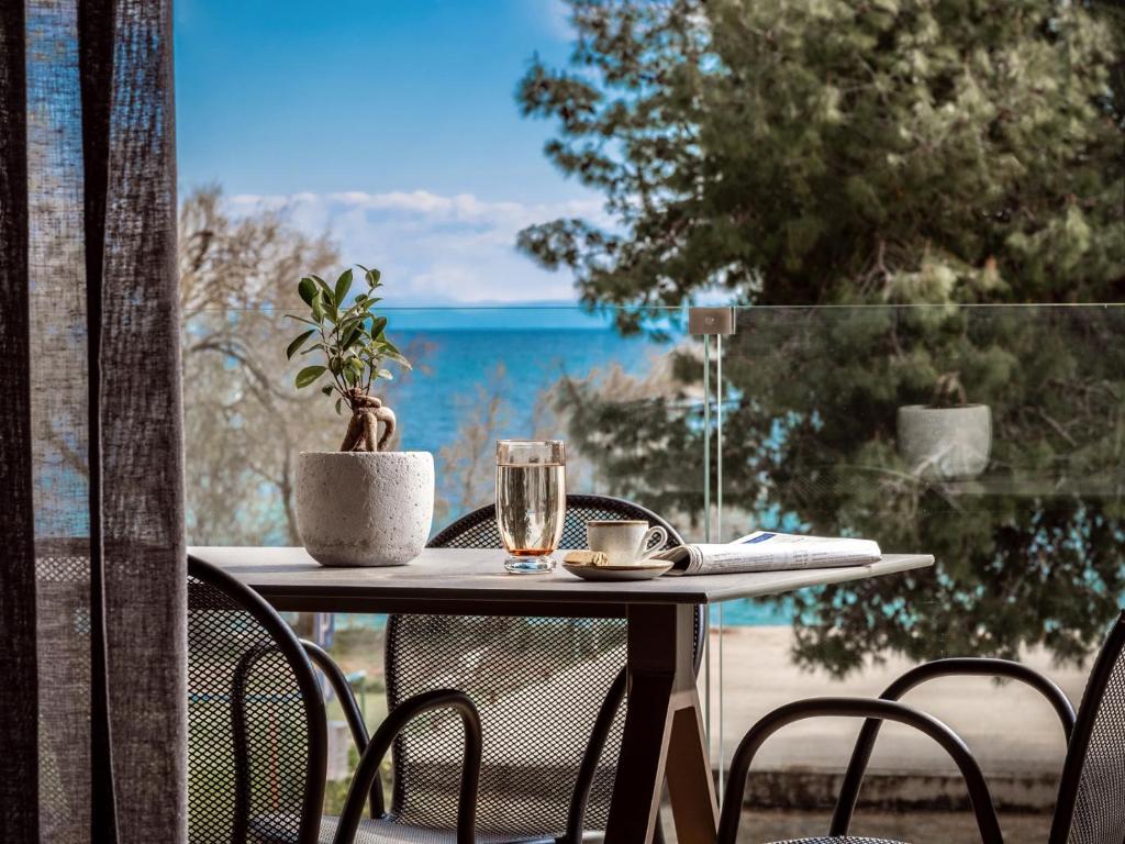 a table with a glass of wine and a plant on a balcony at Point Ephemere Beachfront Apartments in Zakynthos Town