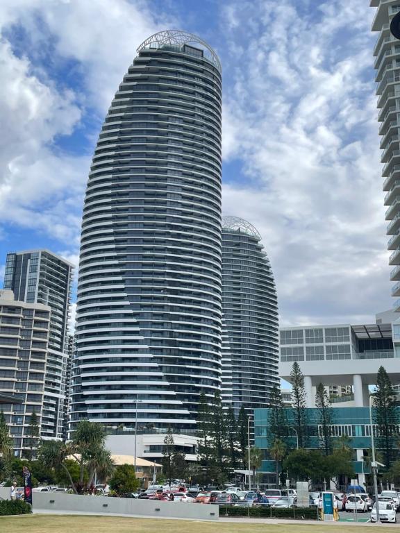 黄金海岸4 Bedroom Huge Sub Penthouse Oracle Level 31 Magnif VIEWS 260m2 Family Skyhome Sleeps 8 Adults and 2 Children, Sofa Bed Portacot, High Chair Central to Everything Resort Skyhome 5 STAR Luxury的一座高楼，前面停着汽车