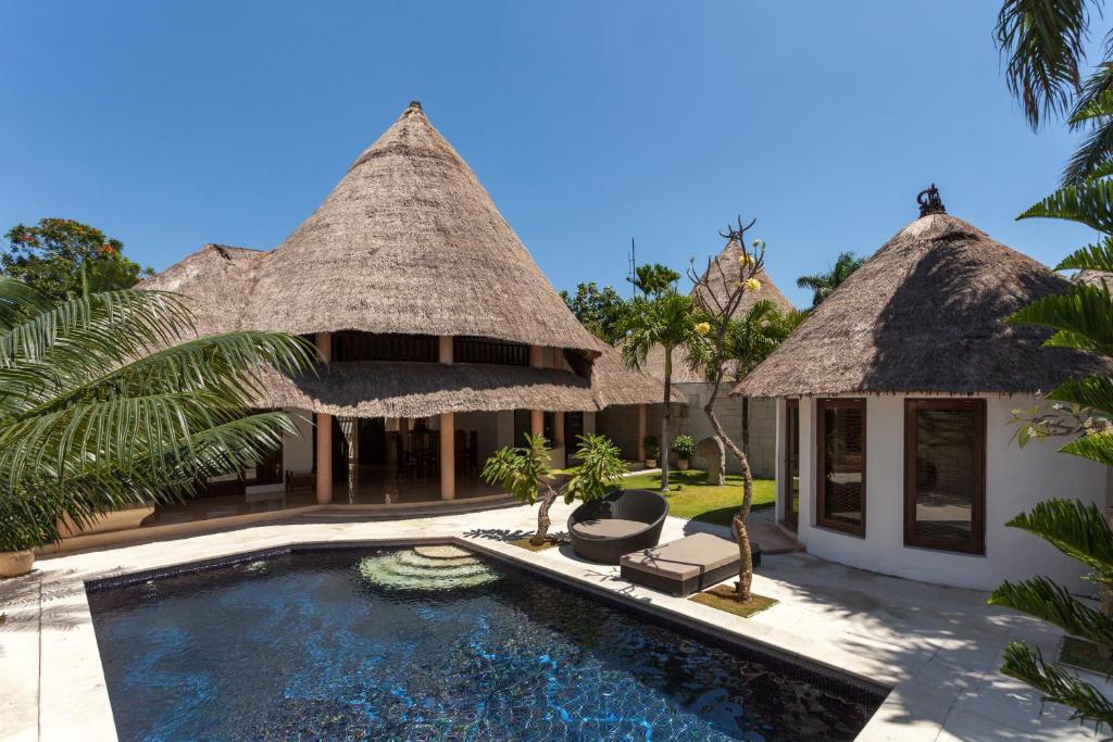 a villa with a swimming pool with a thatch roof at Bvilla Seaside in Seminyak