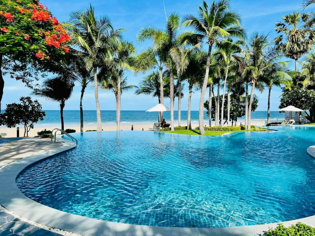 een zwembad naast een strand met palmbomen bij Baan Sanploen Hua Hin- Luxury Two Bedrooms in Hua Hin
