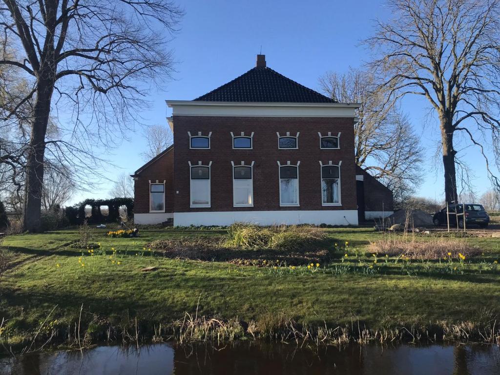 a large brick building on a field with a pond at De kastanjehof 31 in Beerta