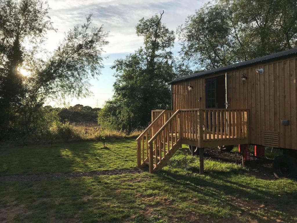 a wooden cabin with a deck in a field at Sunset Shepherds Hut in Taunton