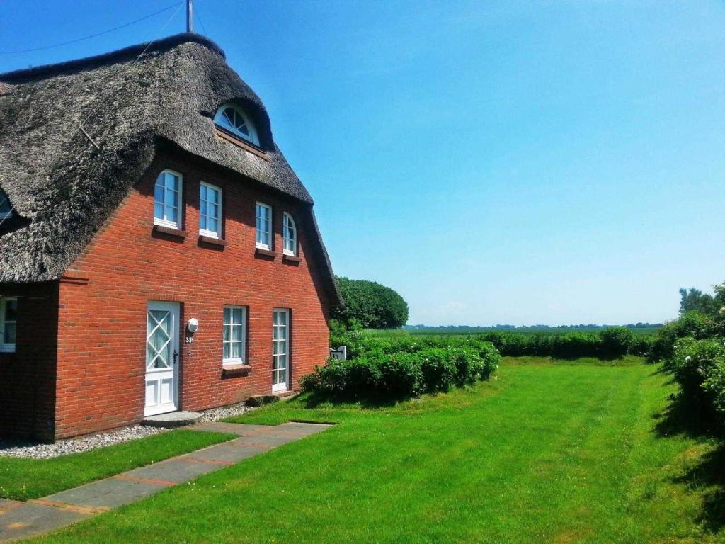 a red brick house with a thatched roof on a green field at Haus am Meer in Nordstrand