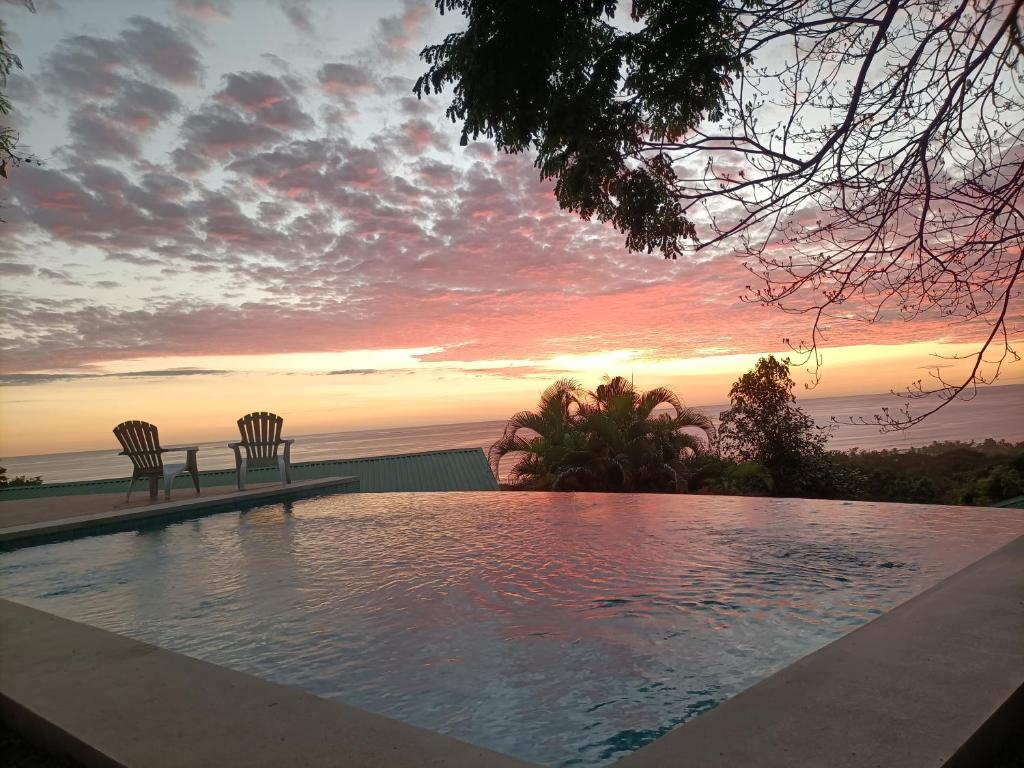a swimming pool with two chairs and a sunset at Vista Naranja Ocean View House in Mal País