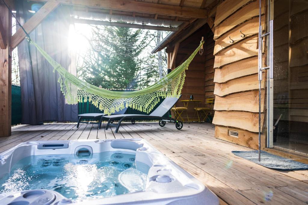 una hamaca en un porche cubierto con bañera de hidromasaje en Charmante Cabane dans les arbres avec jacuzzi et sauna, en Boismorand