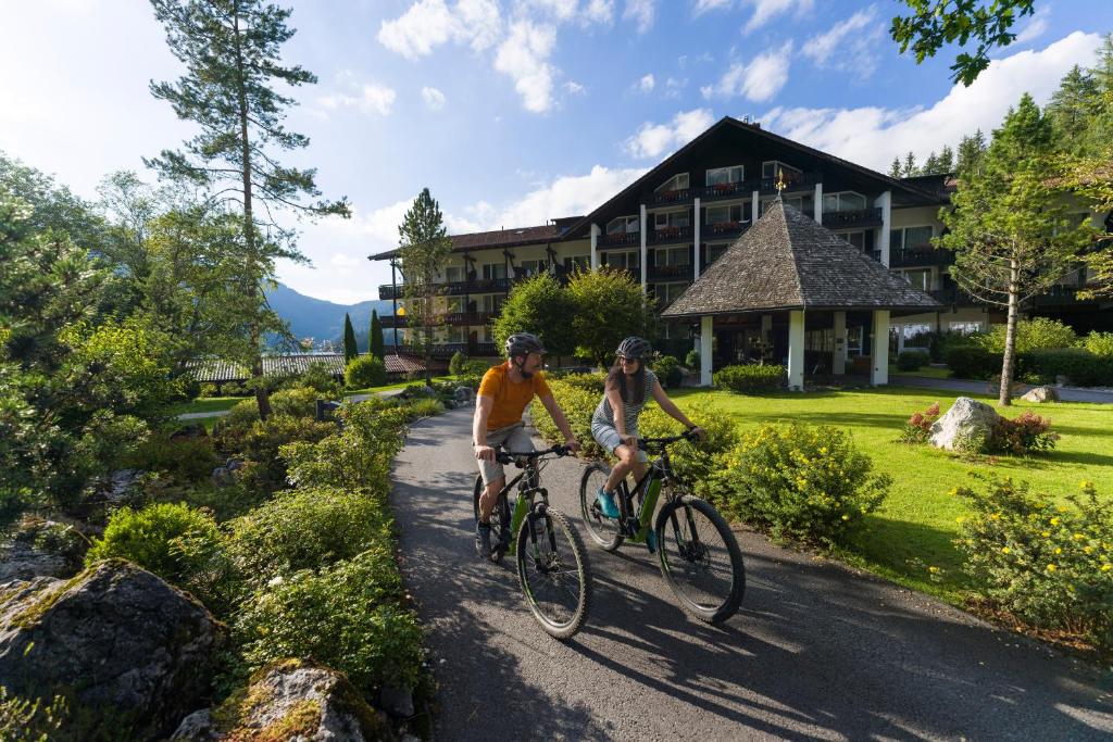 due persone che vanno in bicicletta lungo un sentiero di fronte a una casa di Eibsee Hotel a Grainau