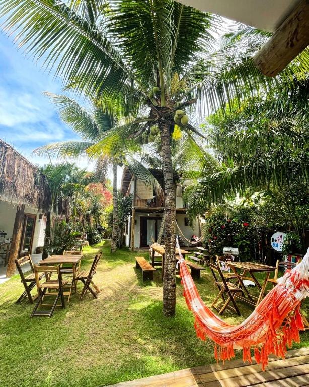 a hammock under a palm tree with tables and chairs at Pousada Jaboticaba Caraíva in Caraíva