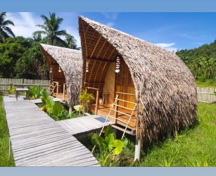 Cabaña con techo de césped y pasarela de madera en Palayan Paradise Huts, en San Vicente