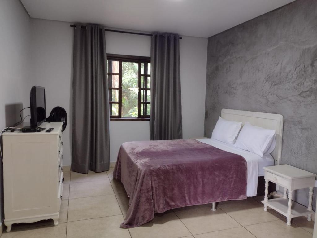 1 dormitorio con 1 cama, TV y ventana en Armazém do Porto Chalé Ixora, en Morretes