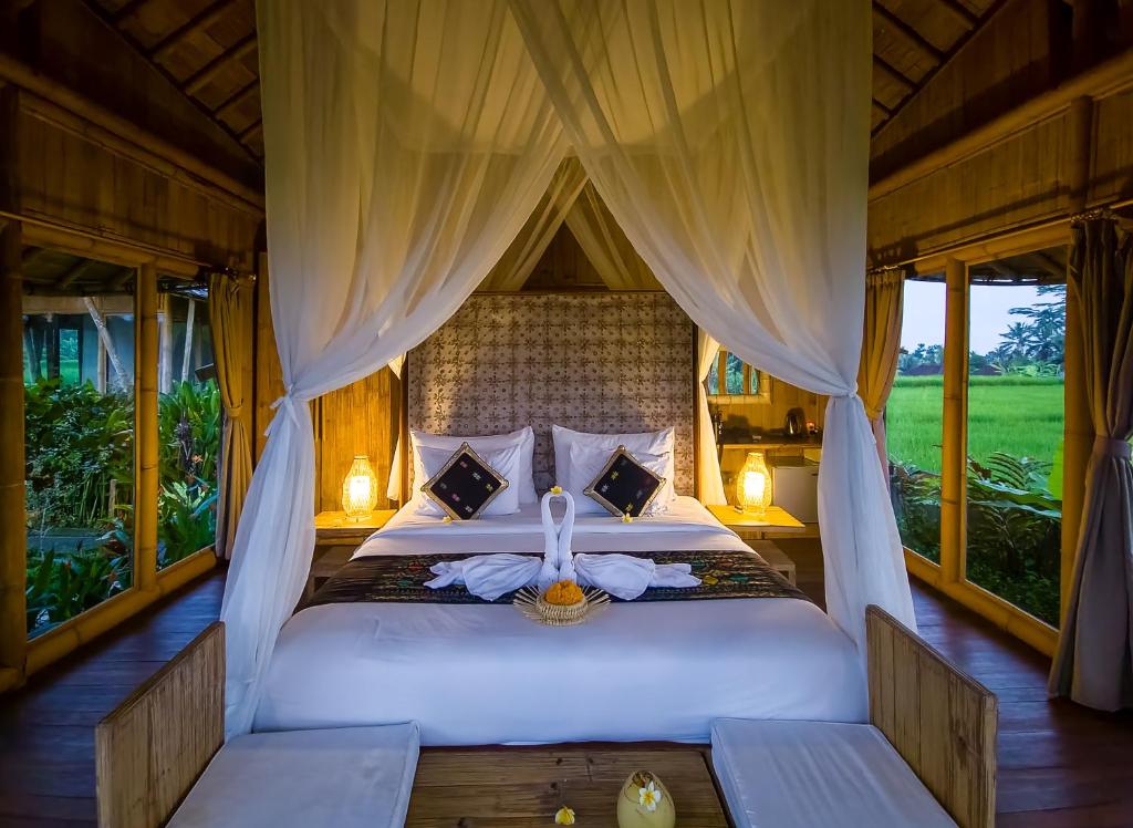 a bedroom with a bed with curtains and windows at Padi Bali Eco Villas in Payangan
