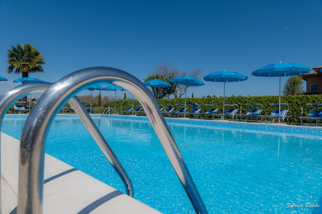 a swimming pool with chairs and blue umbrellas at Albergo Bagner in Sirmione