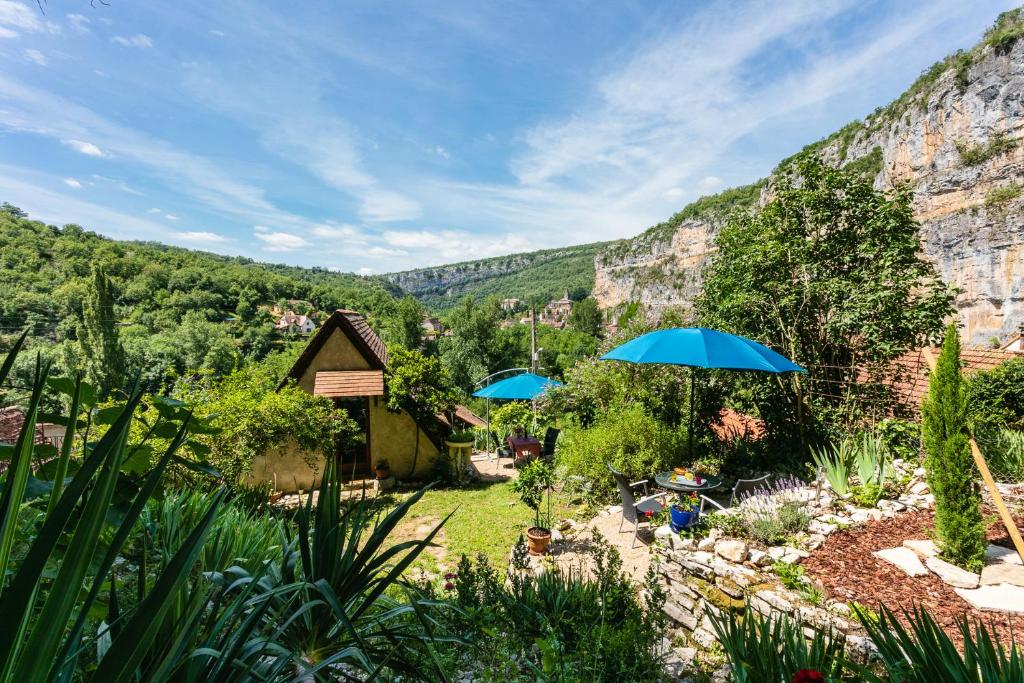 a garden with blue umbrellas in front of a mountain at Gîtes Un Jardin dans la Falaise in Cabrerets