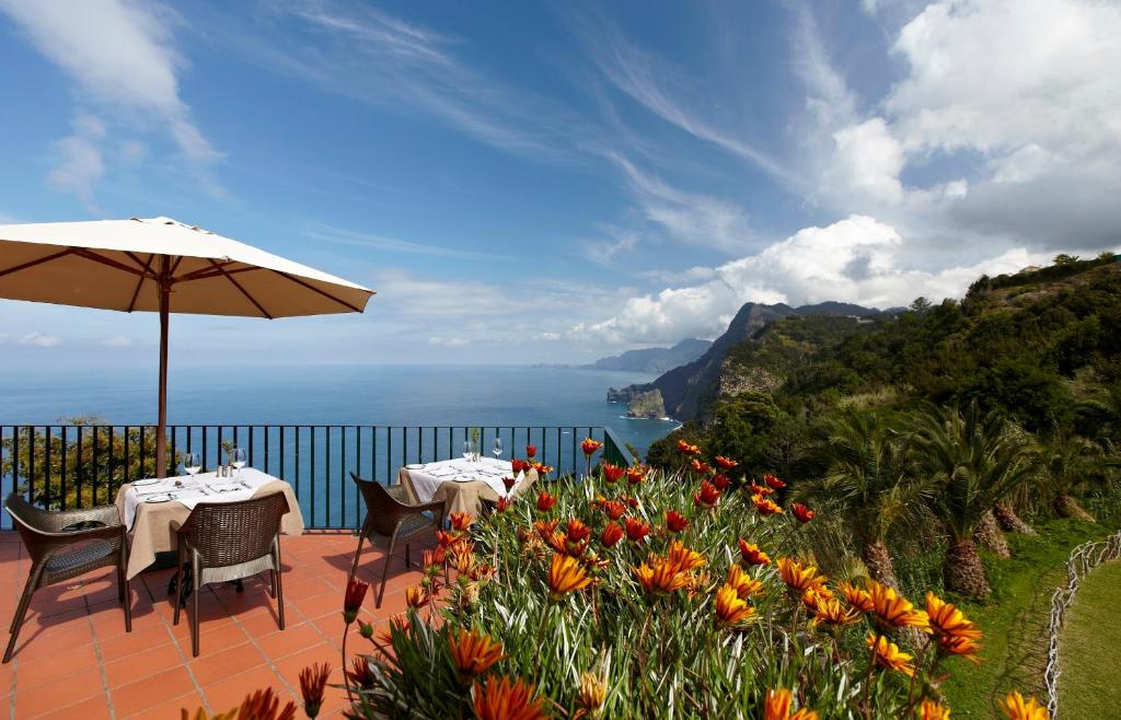 a patio with two tables and an umbrella and flowers at Hotel Quinta Do Furao in Santana